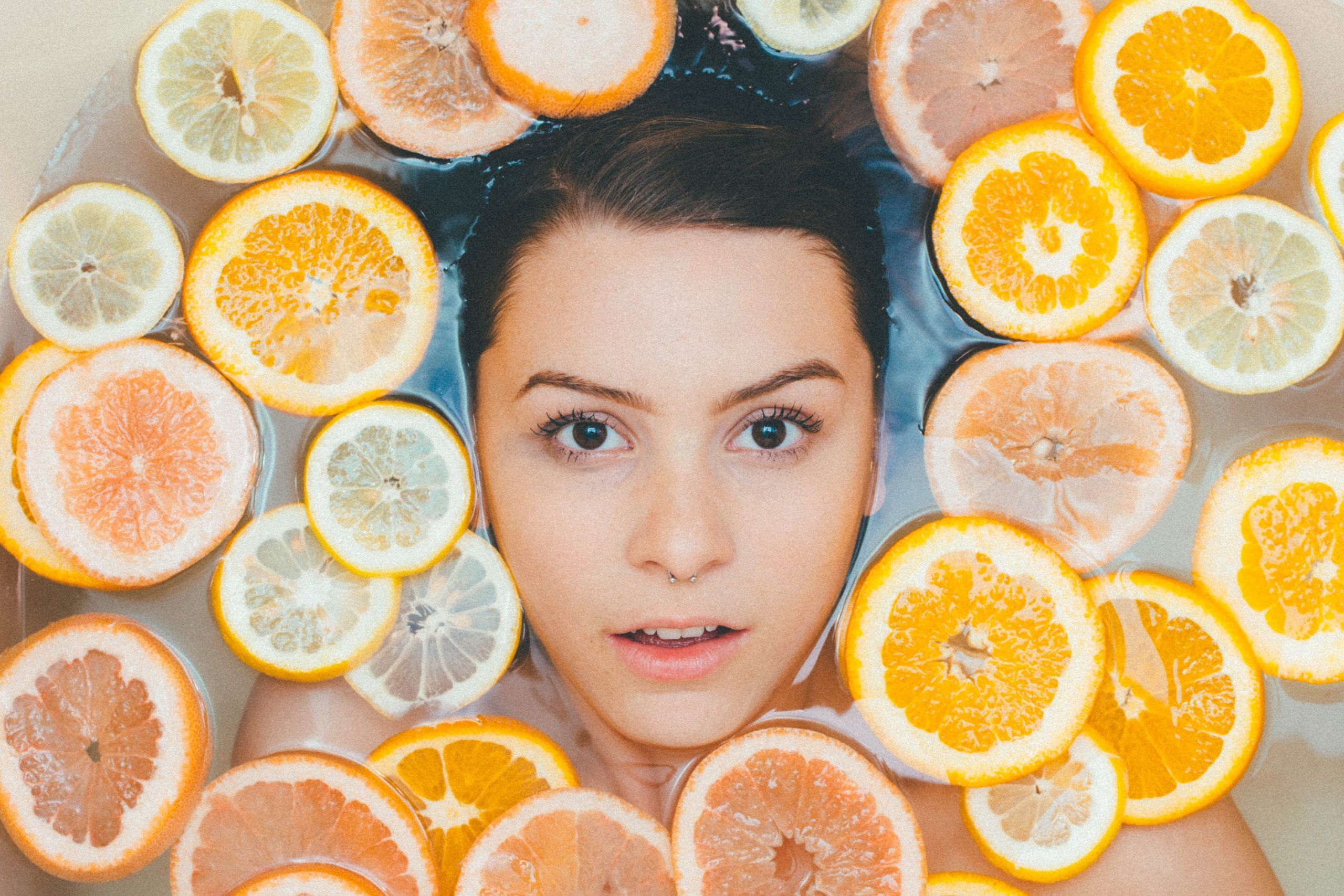 Ladies face in a bath full of sliced citrus fruit floating